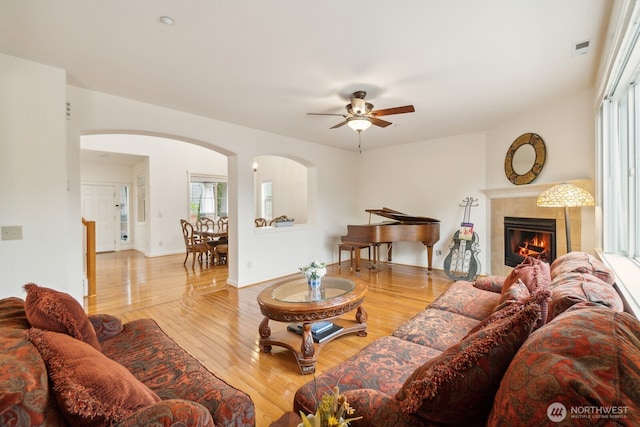 living room featuring a ceiling fan, visible vents, a tiled fireplace, arched walkways, and wood finished floors