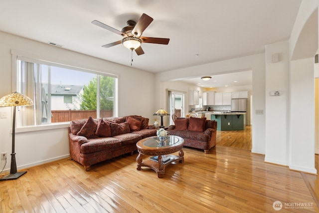 living room with baseboards, ceiling fan, visible vents, and light wood-style flooring