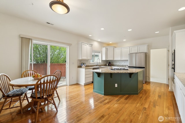 kitchen featuring visible vents, a kitchen island, white cabinets, a sink, and appliances with stainless steel finishes