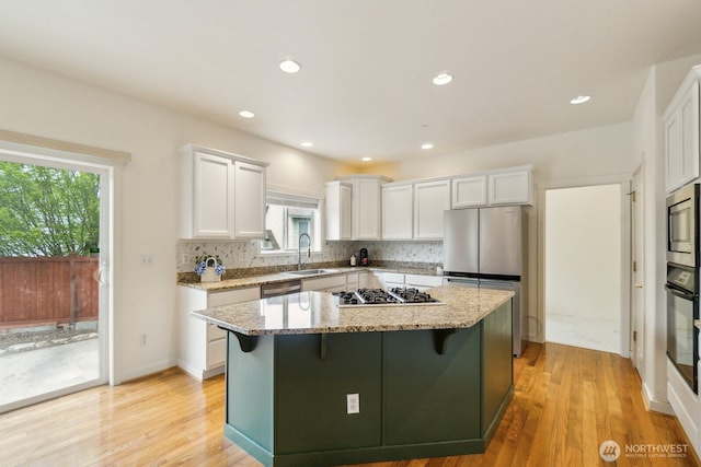 kitchen featuring light stone countertops, a sink, stainless steel appliances, white cabinetry, and a kitchen island