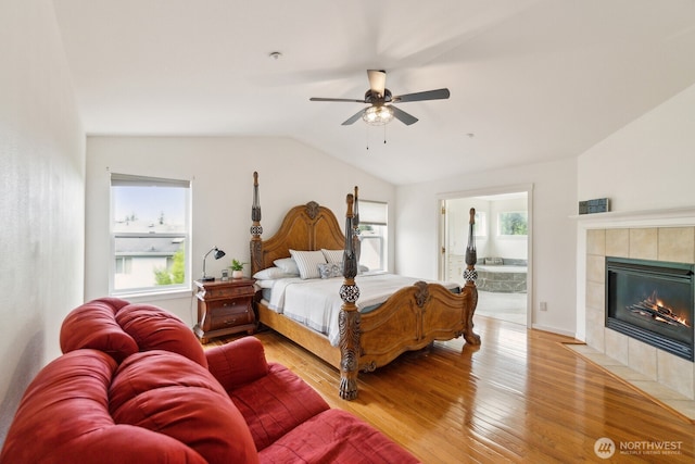 bedroom with light wood-type flooring, ensuite bathroom, vaulted ceiling, and a fireplace