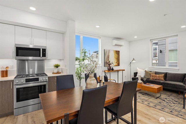 dining area featuring a wall mounted air conditioner, light wood finished floors, and plenty of natural light