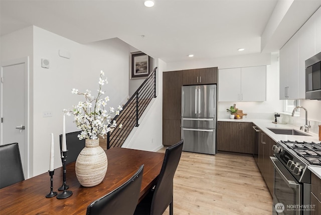 kitchen with dark brown cabinetry, light wood-style flooring, stainless steel appliances, and a sink