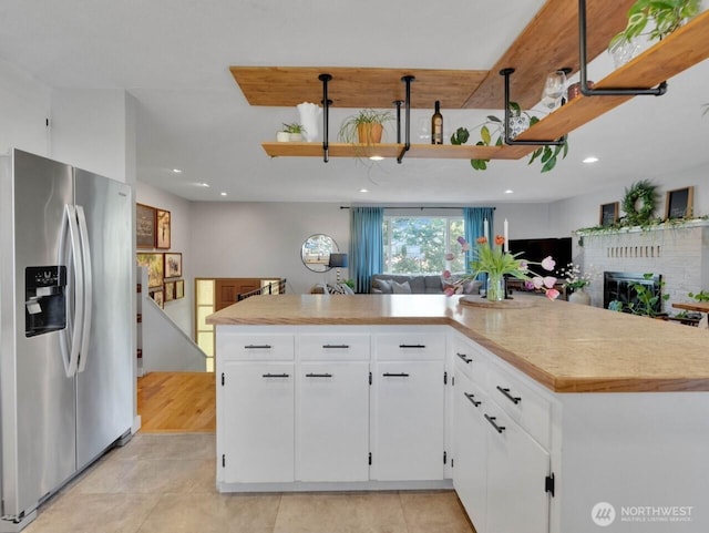 kitchen with light countertops, light tile patterned floors, stainless steel fridge, a fireplace, and white cabinets