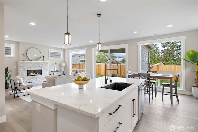 kitchen with a sink, a stone fireplace, a center island with sink, light wood-type flooring, and pendant lighting