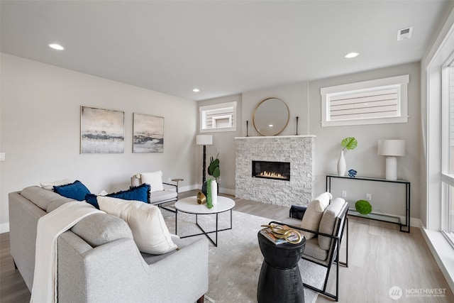 living room with visible vents, wood finished floors, baseboards, a stone fireplace, and recessed lighting