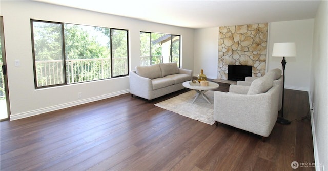 living room featuring dark wood-style floors, a stone fireplace, and baseboards