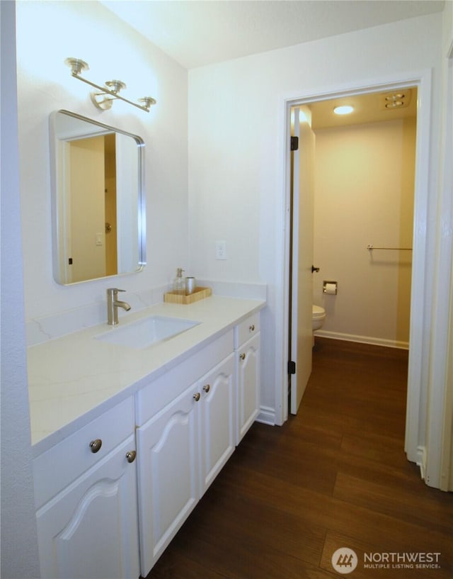 bathroom with wood finished floors, toilet, vanity, and baseboards