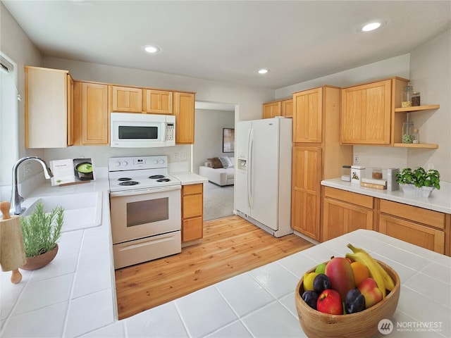 kitchen featuring tile countertops, a sink, light wood finished floors, recessed lighting, and white appliances