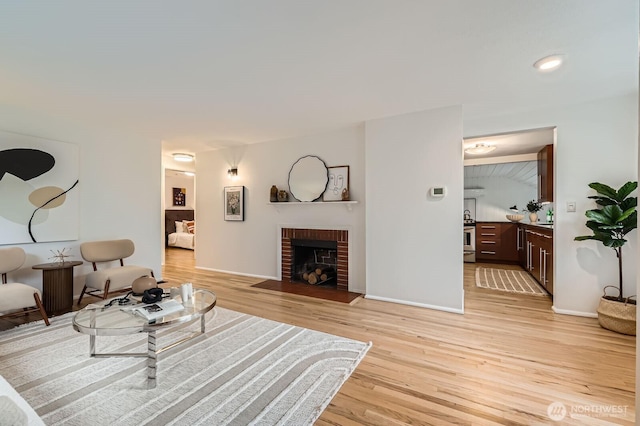 living room featuring baseboards, a brick fireplace, and light wood-style flooring