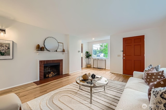 living area featuring baseboards, a brick fireplace, and wood finished floors