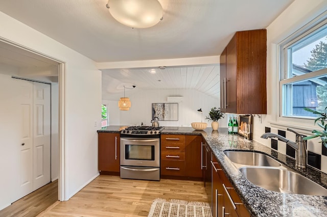 kitchen featuring stainless steel range with gas cooktop, a sink, light wood-style flooring, and dark stone countertops