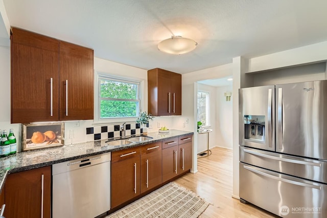 kitchen featuring a sink, light wood-style flooring, dark stone counters, and stainless steel appliances