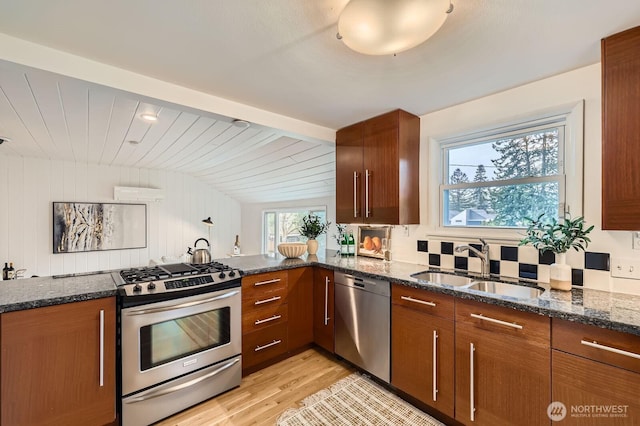 kitchen featuring light wood-type flooring, a sink, dark stone counters, and stainless steel appliances