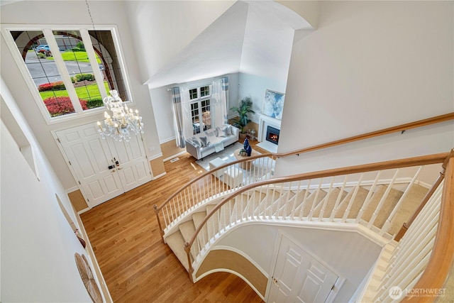 entrance foyer featuring wood finished floors, baseboards, a warm lit fireplace, a high ceiling, and stairs
