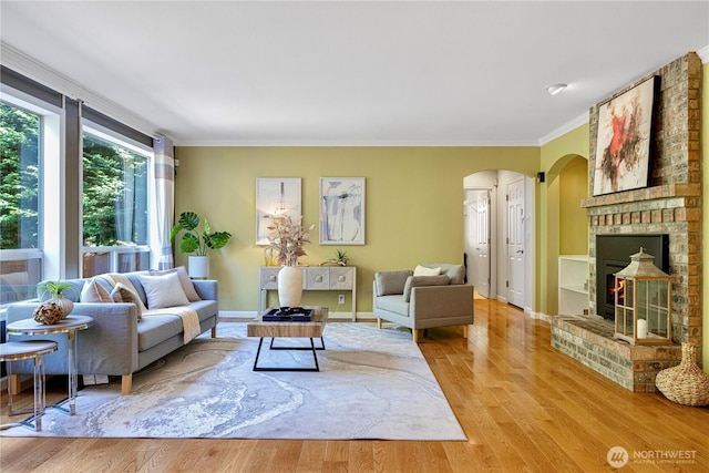 living room with crown molding, arched walkways, a fireplace, and wood finished floors