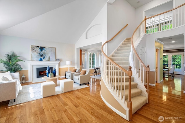living area with wood finished floors, high vaulted ceiling, baseboards, a glass covered fireplace, and stairs