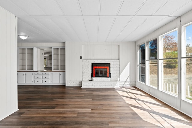 unfurnished living room featuring wood finished floors, a brick fireplace, and wood walls