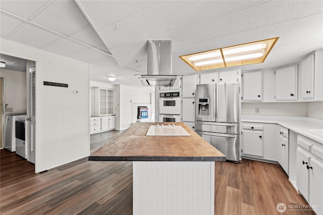 kitchen featuring island exhaust hood, dark wood-style floors, stainless steel fridge with ice dispenser, white double oven, and separate washer and dryer