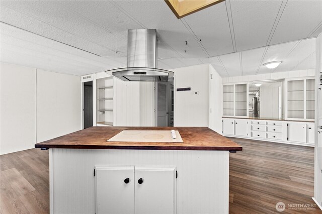 kitchen with white electric stovetop, white cabinetry, island range hood, built in shelves, and wood finished floors