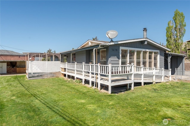 rear view of property featuring board and batten siding, a lawn, fence, and a deck