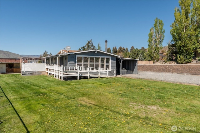 rear view of property with a deck, a sunroom, fence, and a lawn