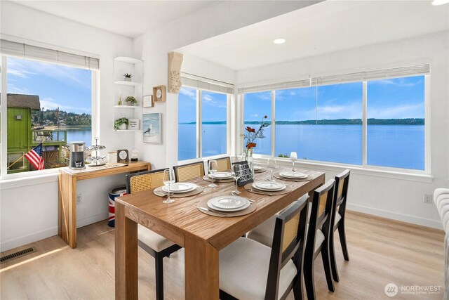 dining area with a water view, light wood-style flooring, and visible vents