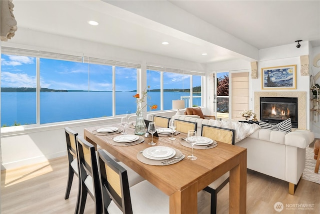 dining space with a premium fireplace, a water view, recessed lighting, and light wood-style floors