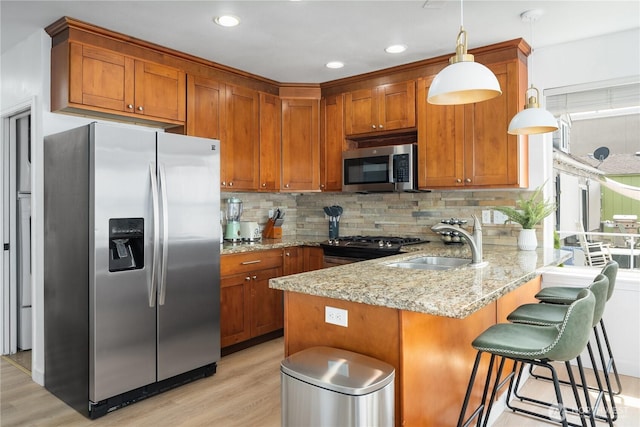 kitchen featuring a sink, light wood finished floors, brown cabinetry, stainless steel appliances, and a peninsula