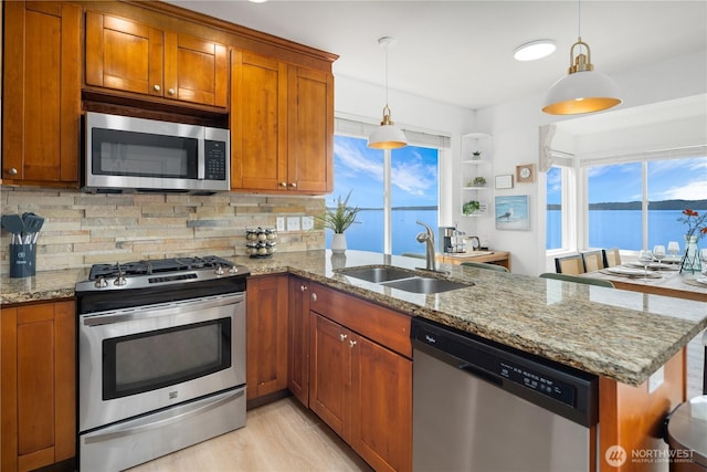 kitchen featuring decorative backsplash, a peninsula, brown cabinets, a sink, and appliances with stainless steel finishes