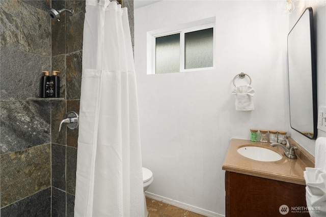 bathroom with vanity, baseboards, a tile shower, and toilet