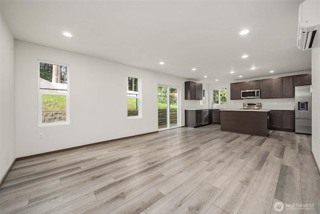 unfurnished living room with light wood finished floors, a sink, baseboards, recessed lighting, and a wall mounted air conditioner