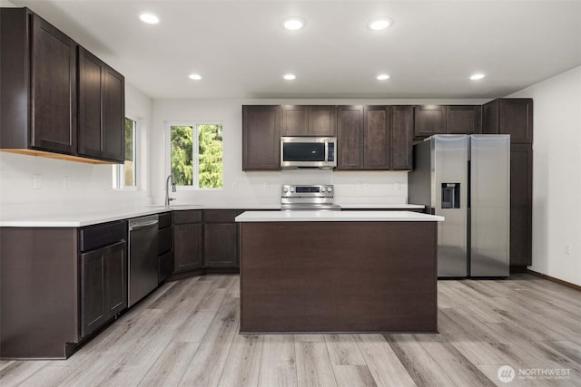 kitchen with dark brown cabinetry, a sink, light wood-style floors, and appliances with stainless steel finishes