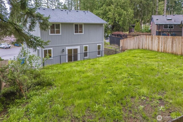 rear view of house with a yard, roof with shingles, and fence