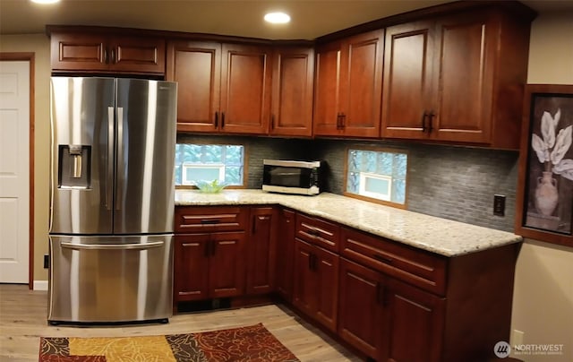 kitchen with light wood-style flooring, appliances with stainless steel finishes, backsplash, and light stone countertops