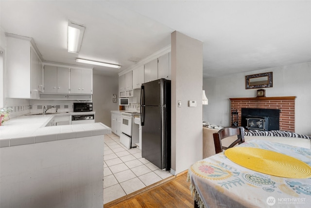 kitchen with tile countertops, black appliances, open floor plan, light wood-type flooring, and a brick fireplace