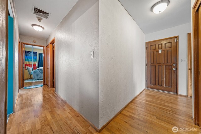hallway featuring light wood-style flooring, visible vents, baseboards, and a textured wall