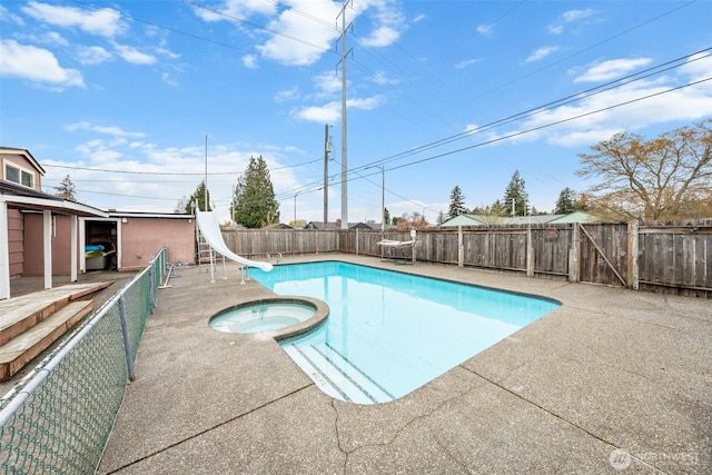 view of swimming pool with a water slide, a pool with connected hot tub, a patio area, and a fenced backyard
