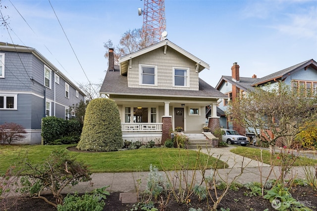 view of front of house featuring a porch, a chimney, roof with shingles, and a front lawn