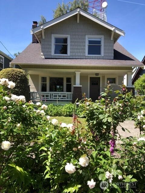 bungalow-style home with roof with shingles, covered porch, and a chimney