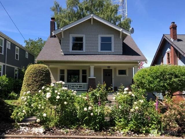bungalow-style house featuring roof with shingles, a chimney, and a porch