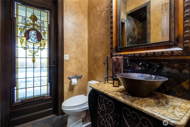 half bathroom featuring toilet, a textured wall, and vanity