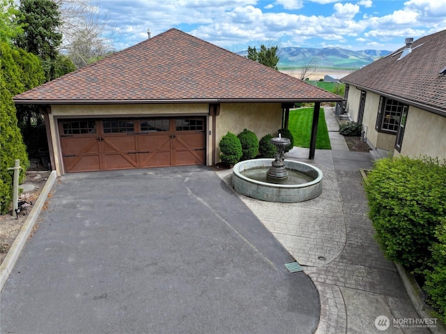view of front facade featuring stucco siding, aphalt driveway, a shingled roof, a mountain view, and an attached garage