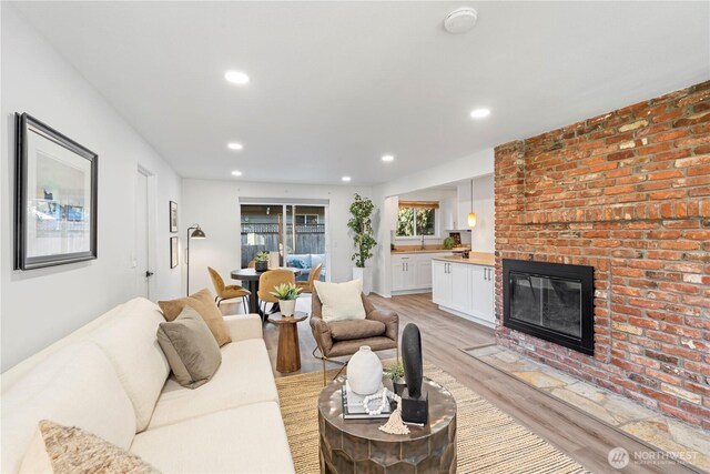 living room with a brick fireplace, light wood finished floors, and recessed lighting