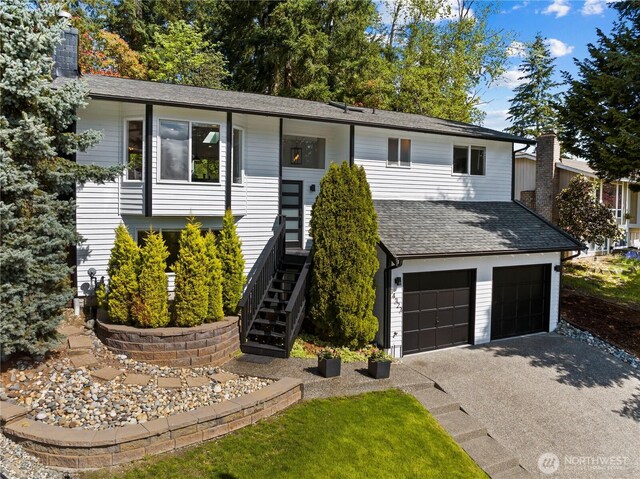 raised ranch featuring an attached garage, a chimney, driveway, and stairs