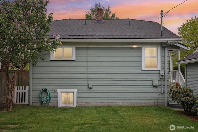 back of property at dusk with a shingled roof and a chimney