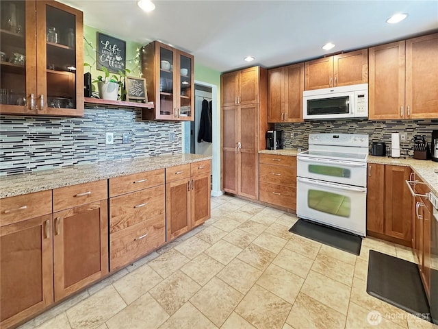 14914 20th Ave E, Parkland, WA 98445 - kitchen featuring glass insert cabinets, brown cabinetry, white appliances, light stone counters, and backsplash