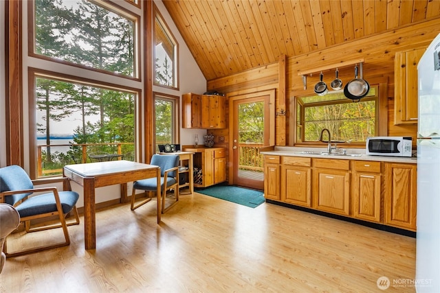 kitchen with a sink, light countertops, white microwave, wooden walls, and light wood-style floors