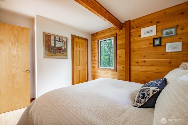 bedroom with wooden walls, beamed ceiling, and wood finished floors