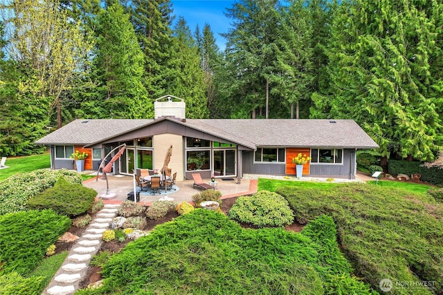 rear view of property with a shingled roof, a chimney, and a patio